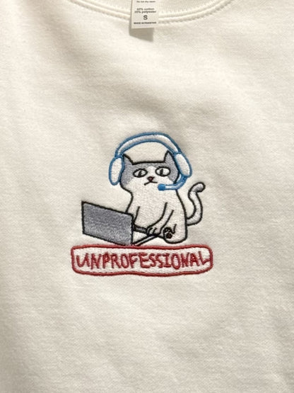 Close-up photo showing the result of the embroidery depicting a cute cartoon grey and white cat wearing headphones and using a laptop looking confused with "UNPROFESSIONAL" crudely stamped below it