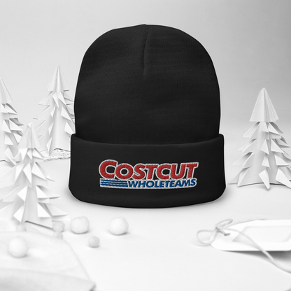 A black beanie with red and blue text "Cost cut whole teams" embroidered in the style of the "Costco Wholesale" logo, on a festive winter background surrounded by pine trees